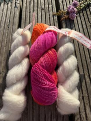 Handgefärbtes Petit-Provence-Garnset „Farbenfreude“ von Herzfasern. In der Mitte liegt ein Strang Herzfasern No. 11 „Petras Farben 2.0“ in leuchtendem Pink, Neonpink und Orange. Links und rechts befinden sich naturfarbene Stränge Herzfasern No. 93 aus Kas